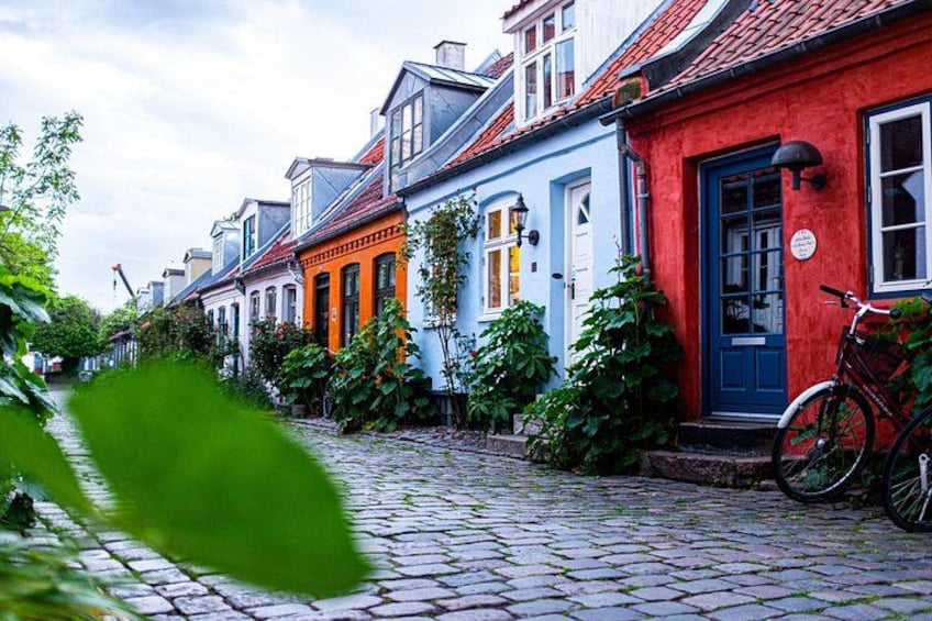 A cobblestone street lined with colorful houses, a bicycle, and greenery. 1