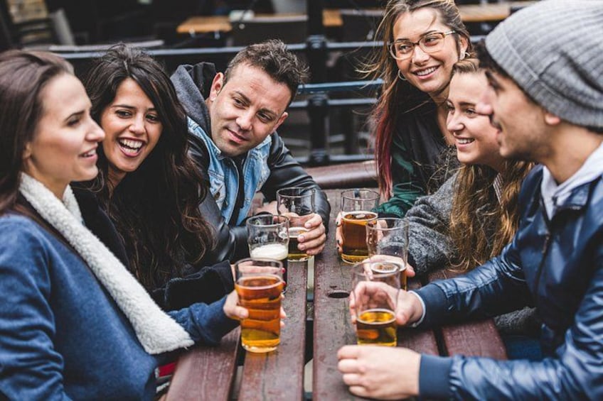 A group of people sitting around a wooden table, holding glasses of beer. 2
