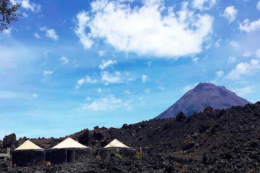 A volcanic landscape with a prominent mountain, three small huts, and a clear sky. 1