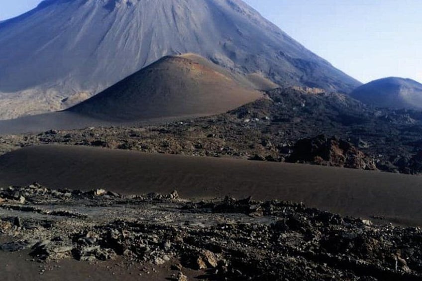 A volcanic landscape with a prominent mountain, a flat lava field, and scattered rocks. 5