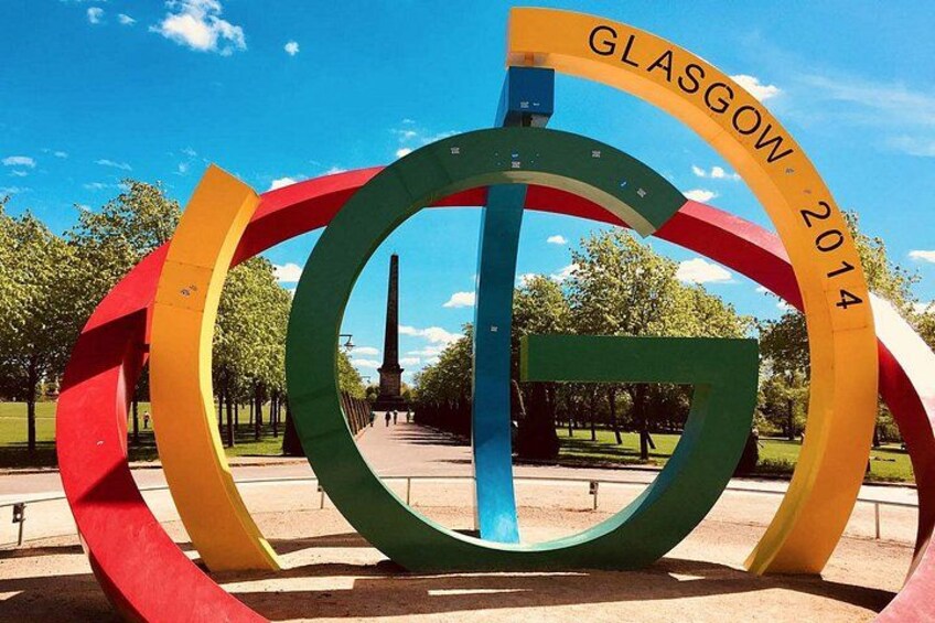 A colorful sculpture with the text 'GLASGOW 2014' in a park with trees and a monument in the background. 5