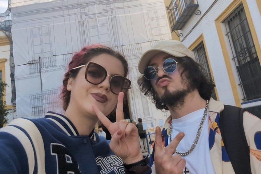 Two people making peace signs in front of a building with architectural details. 4