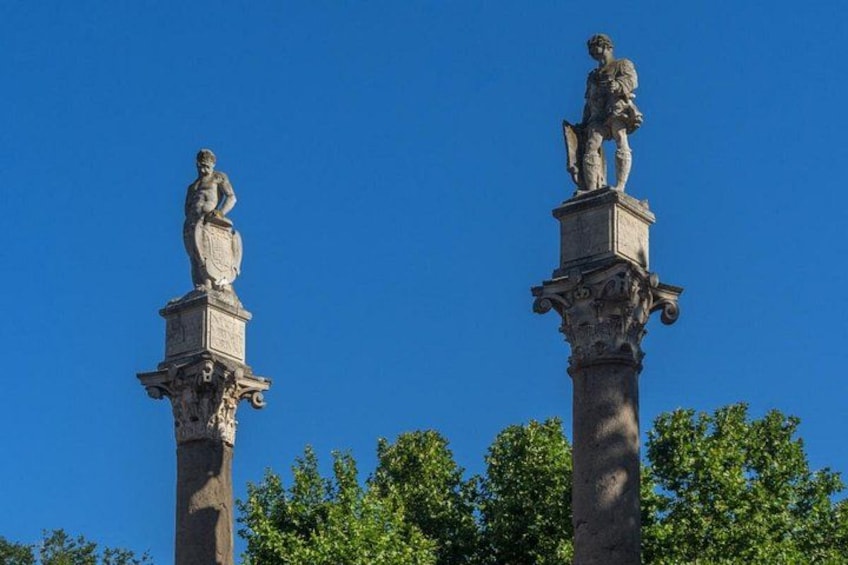 Two statues on tall columns against a clear blue sky. 3