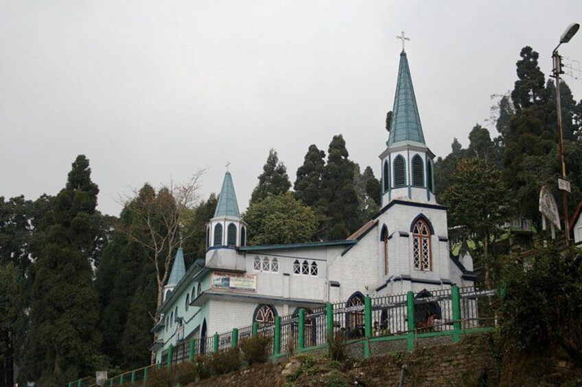 A church with a green spire and white walls, surrounded by trees. 3