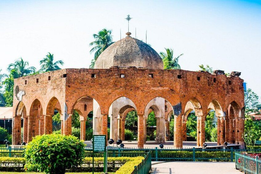 A brick structure with a dome and arches, surrounded by greenery and palm trees. 3
