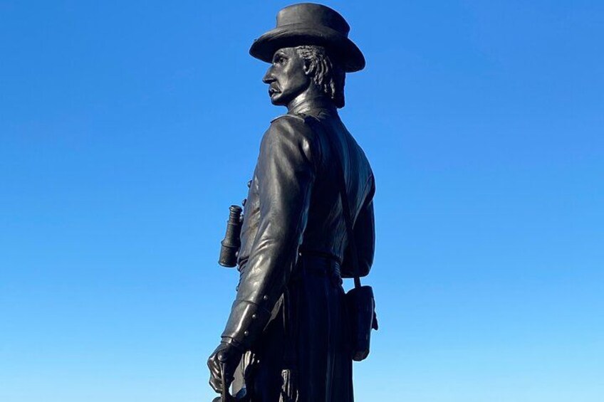 Estatua de un hombre con traje y sombrero, sosteniendo un arma, contra un cielo azul despejado. 3
