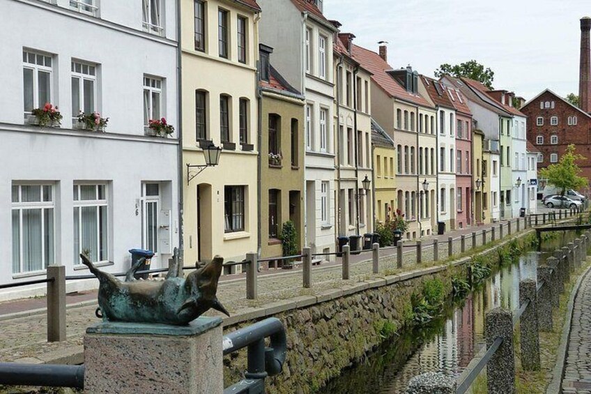 En kanal med bygninger langs den ene side og en statue i forgrunden. 3
