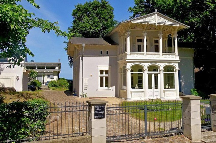 A white building with a balcony, surrounded by a metal fence and greenery. 3
