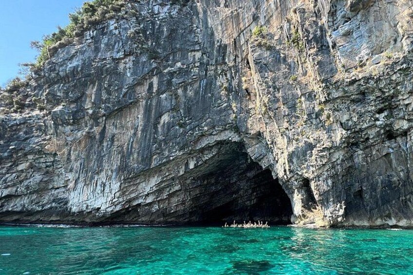 A rocky cliff with a cave entrance and clear turquoise water. 4