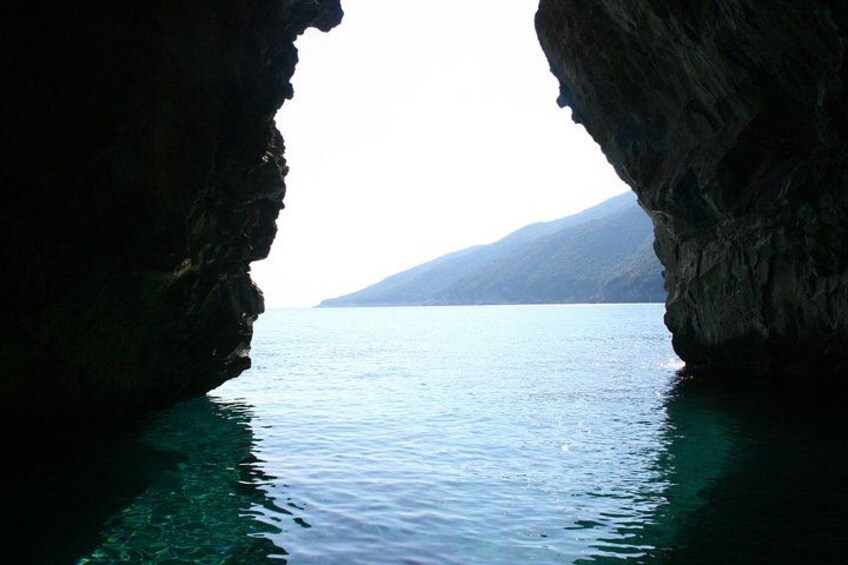 A coastal cave opening with clear water and distant mountains. 3