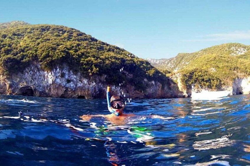 A person snorkeling in clear blue water with rocky cliffs in the background. 2