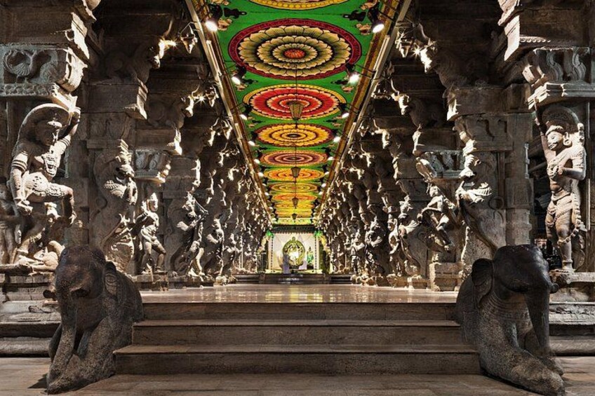 A temple interior with stone carvings, a central deity statue, and a colorful ceiling. 2