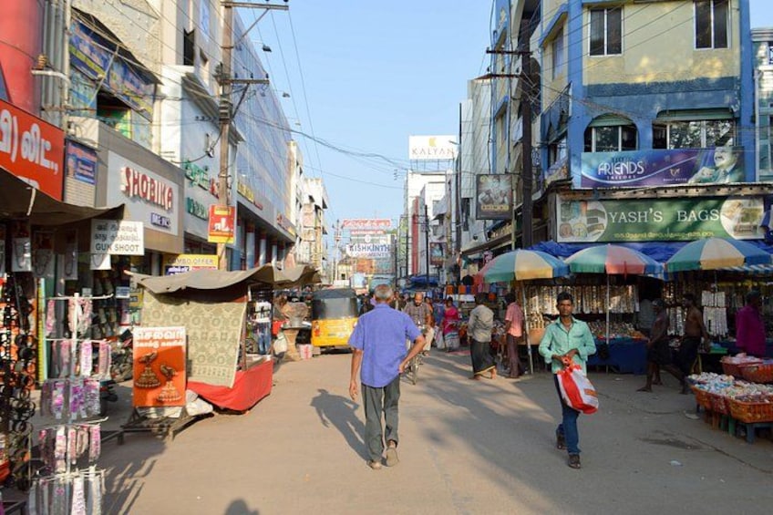 A busy street with shops, a man walking, and a vendor selling fruits. 1