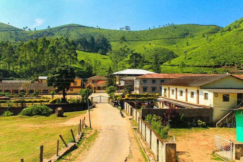 A rural village with houses, a dirt road, and lush green hills in the background. 4