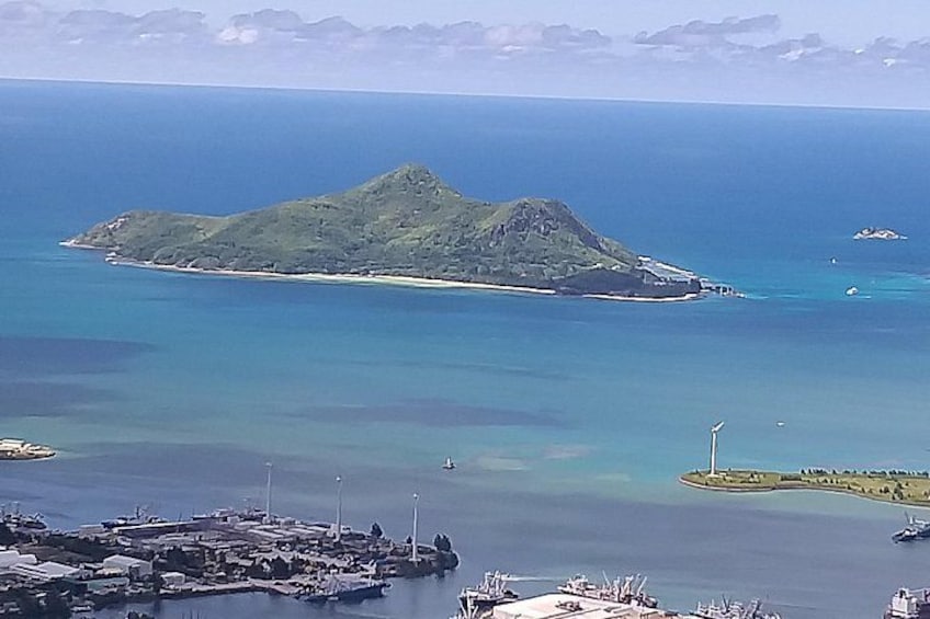 A coastal landscape with a prominent island, a marina with boats, and a clear blue sea. 1