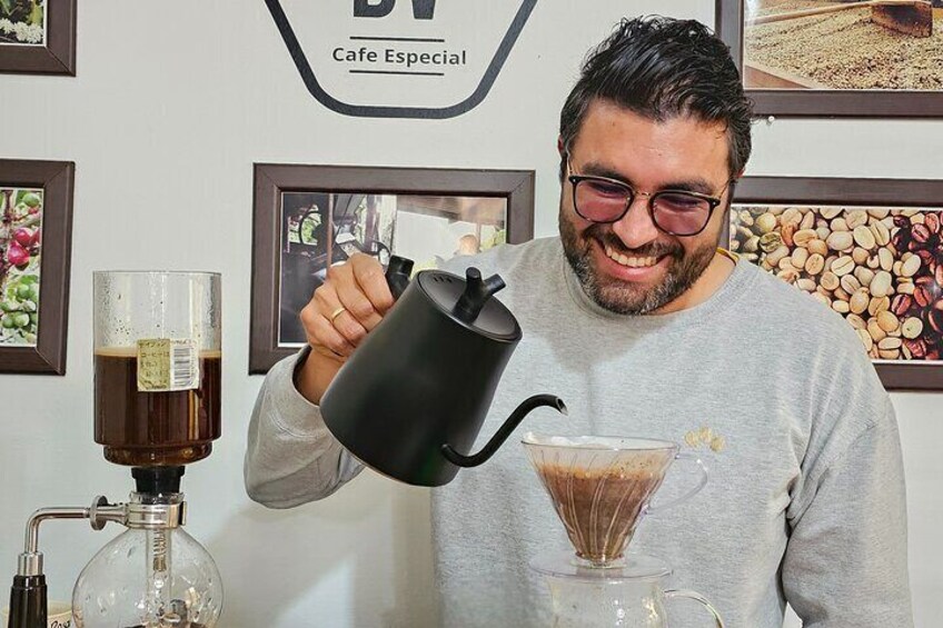 A person pouring a dark liquid into a glass, with a coffee machine and coffee beans in the background. 2