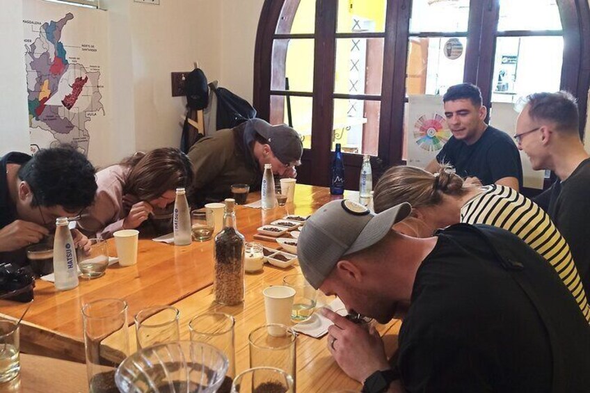A group of people sitting at a wooden table with various bottles and glasses, likely in a café or restaurant setting. 4