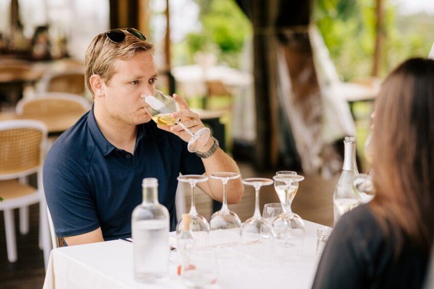 Een persoon drinkt uit een glas aan een buitentafel, met verschillende wijnflessen en -glazen. 5