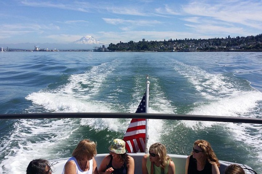 A boat with passengers, an American flag, and a view of a mountain and city skyline across the water. 5