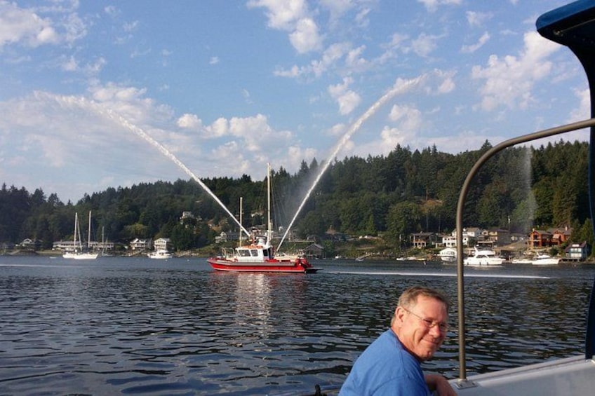 A red boat with water jets, a man in a blue shirt, and a forested shoreline with houses. 4