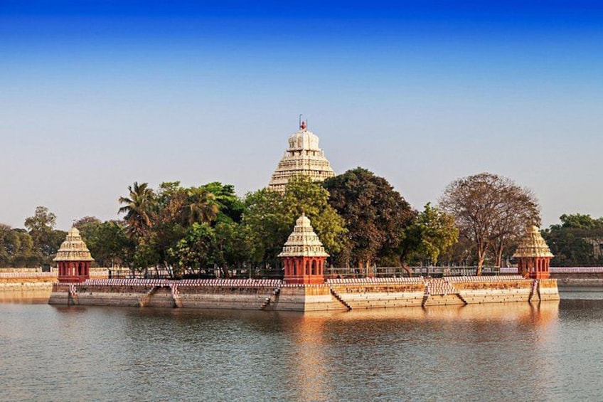 A temple complex with a large central structure and smaller surrounding buildings, a body of water in the foreground, and trees in the background. 3