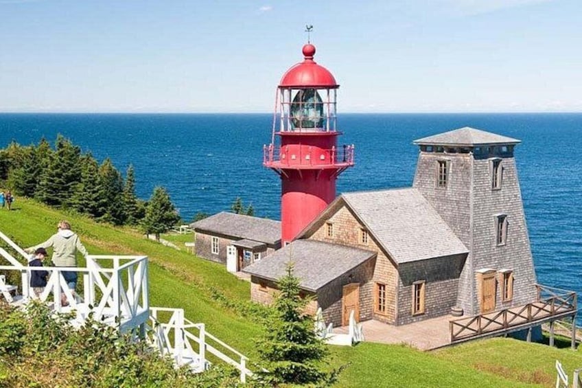 Een rode vuurtoren, een stenen gebouw en een grasheuvel met uitzicht op de oceaan. 2