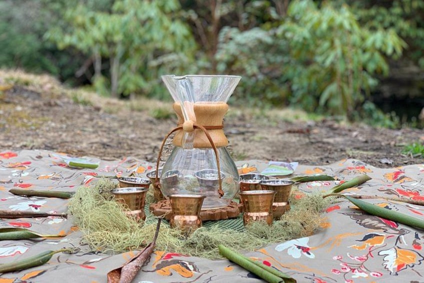 A traditional coffee brewing setup outdoors with a cloth table, a glass filter, and metal cups. 5