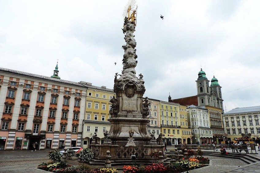 A historic fountain with intricate sculptures, surrounded by a flower bed, in a square with classical architecture and a church in the background. 3