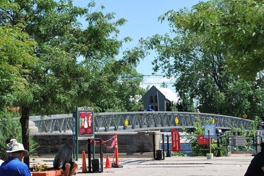 A pedestrian bridge with a metal railing, trees, and a building in the background. 2