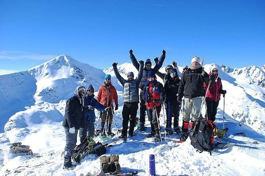 Un groupe de personnes se trouve sur une montagne enneigée, équipées de skis et de planches à neige, et se tient au sommet d’une montagne recouverte de neige. 5
