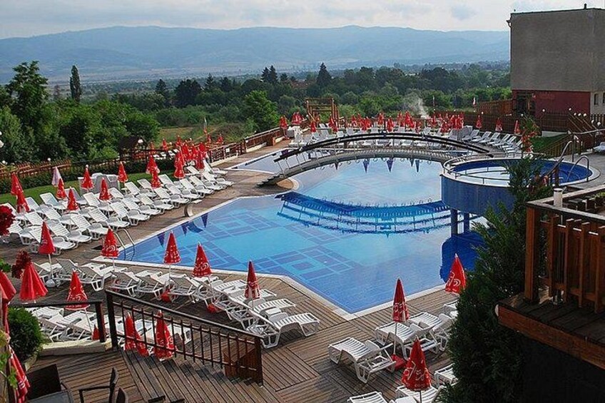 A swimming pool with lounge chairs and umbrellas, surrounded by a deck and a view of mountains. 3