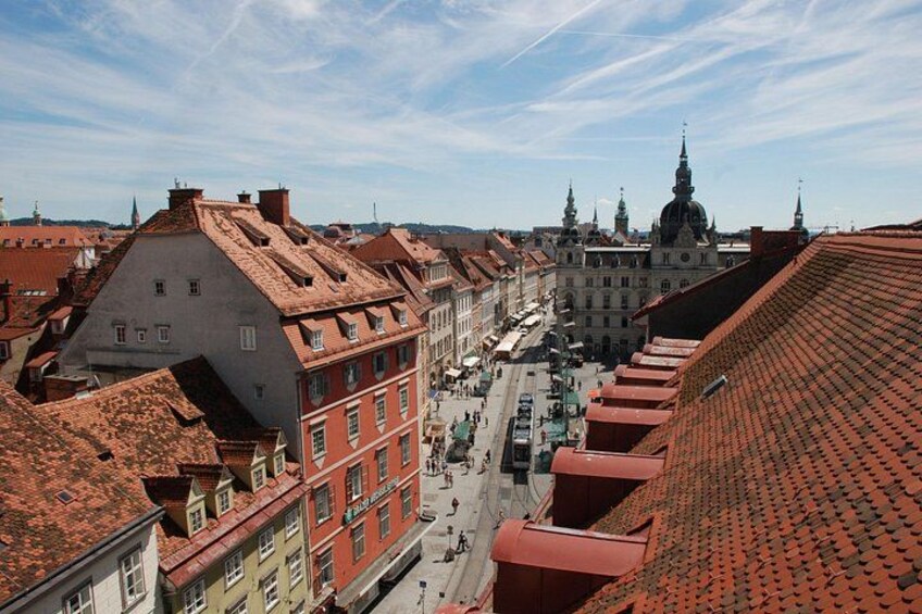 A cityscape with red-tiled roofs, historic buildings, and a prominent church spire. 5