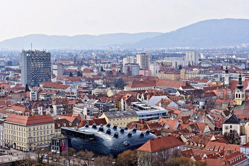 A cityscape with a prominent modern building, traditional architecture, and a mountainous backdrop. 4