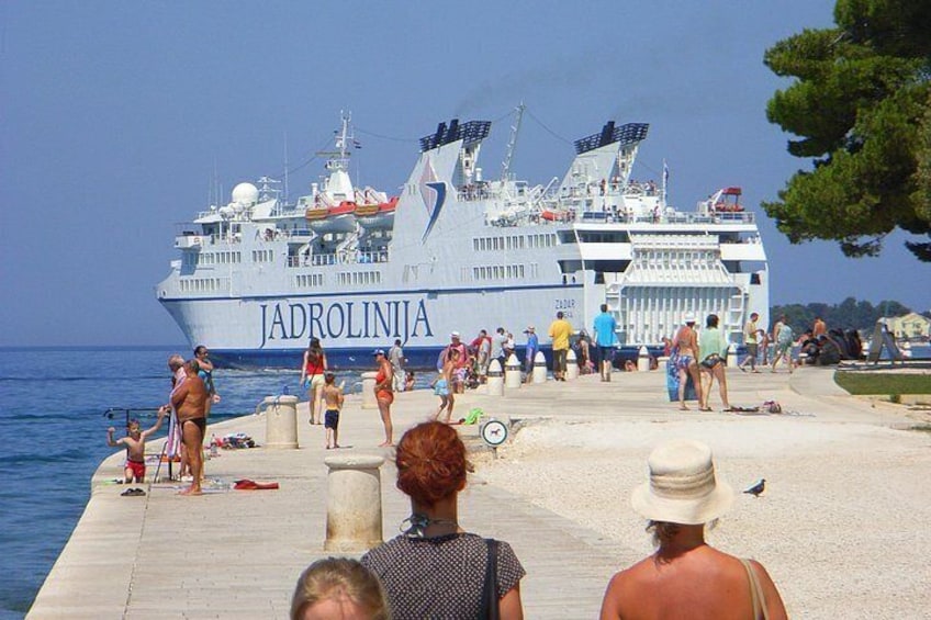 Un grand navire de croisière, le « Jadrolinja », s’est amarré à un quai où se trouvaient des gens qui se promenaient et qui étaient debout. 4