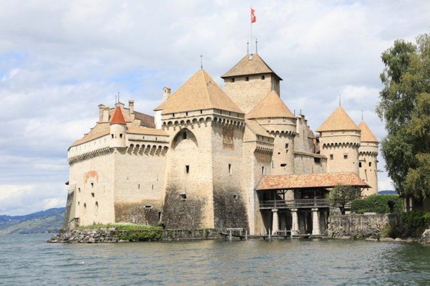 A castle by a lake with multiple towers and a flag. 2
