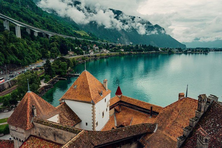 A mountainous landscape with a river, a bridge, and traditional buildings with red-tiled roofs. 1