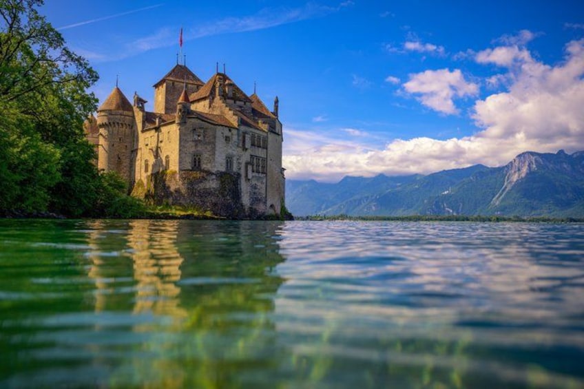 A castle by a lake with mountains in the background. 3