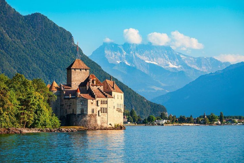 A castle by a lake with mountains in the background. 1