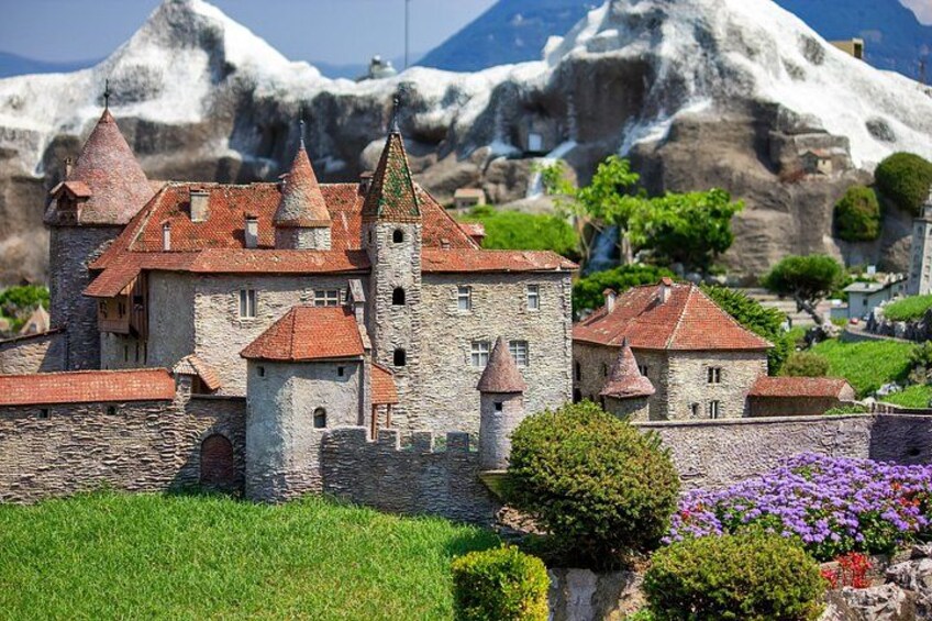 A castle with red-tiled roofs, surrounded by greenery and purple flowers. 4