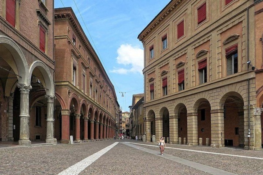 Eine Kopfsteinpflasterstraße gesäumt von historischen Gebäuden mit Rundbogenfenstern und roten Fensterläden. 1