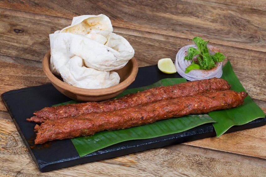 A plate of kebabs, a bowl of flatbread, and a small bowl of salad on a wooden table. 2