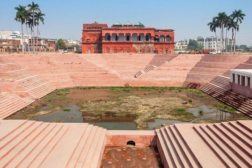 A large open square with a central water body, surrounded by tiered brick structures and palm trees. 4