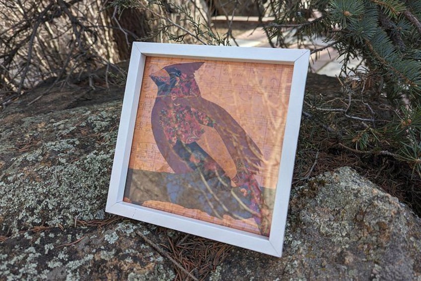 A framed artwork on a rock with lichen, pine branches, and a tree in the background. 2