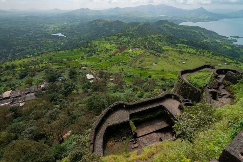 A historical stone structure with a curved wall, surrounded by lush green hills and a lake in the background. 5