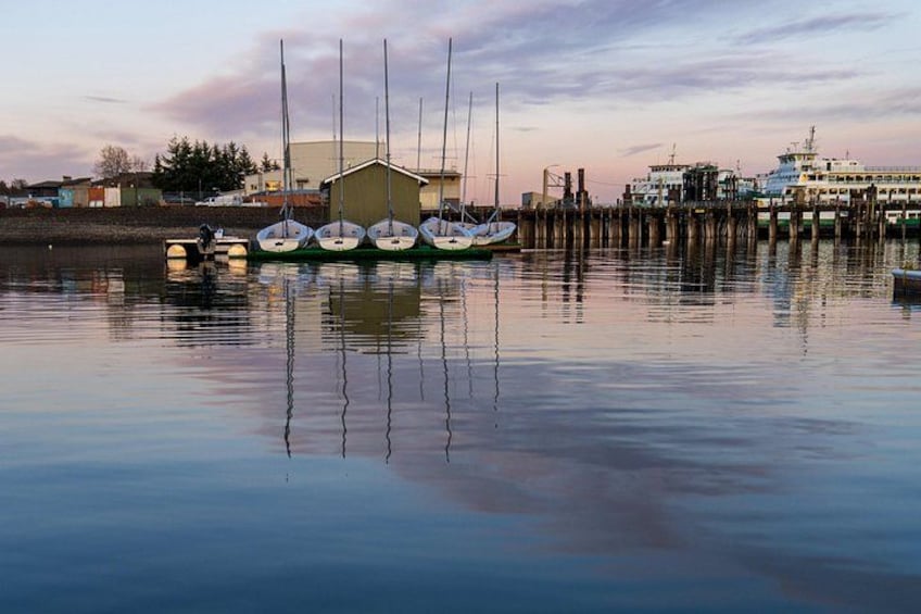 Un puerto tranquilo con varios veleros amarrados, un edificio y un muelle que se adentra en el agua. 2