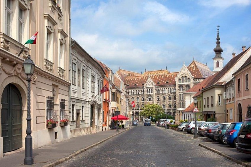 A cobblestone street lined with historic buildings, a church steeple, and parked cars. 2