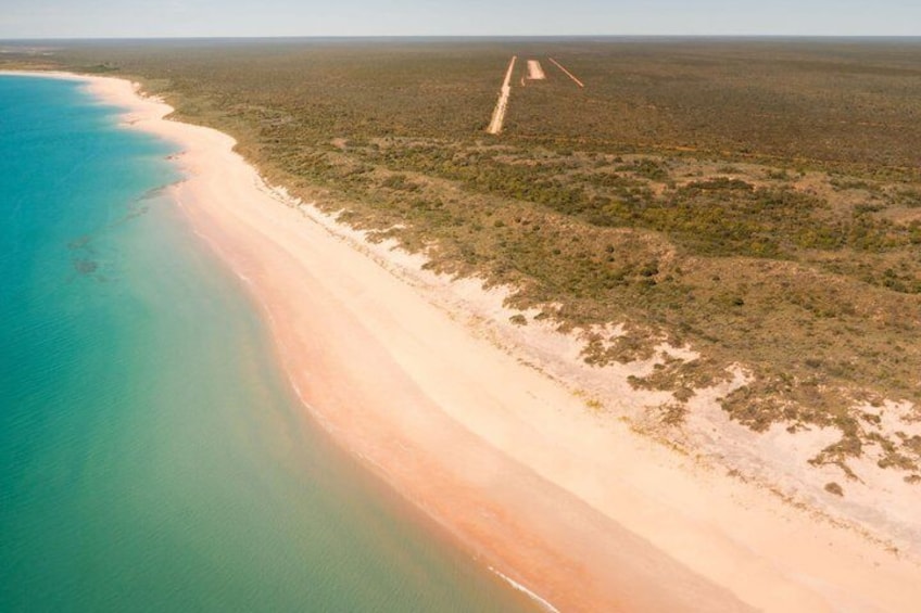 Et kystlandskab med en sandstrand, klart turkis vand og sparsom vegetation. 5