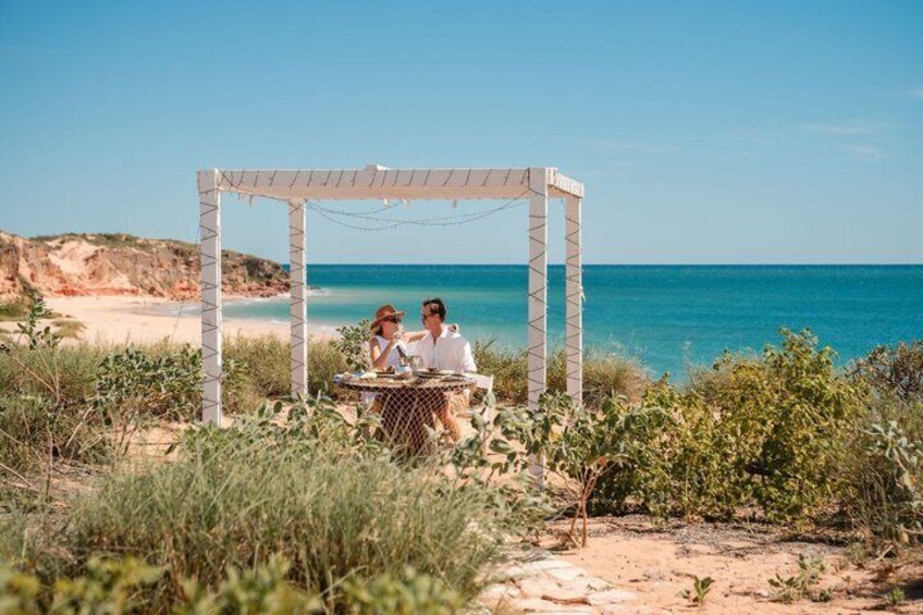 Et par spiser middag under en hvid pergola på en strand med havudsigt. 4
