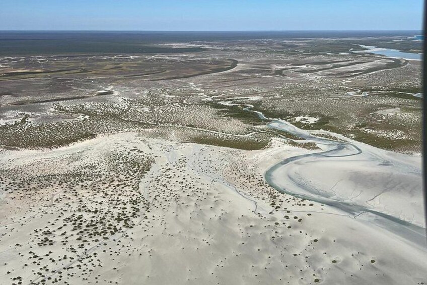 Un vaste paysage désertique, avec une rivière sinueuse, une végétation clairsemée et des étendues d’eau à l’horizon. 4