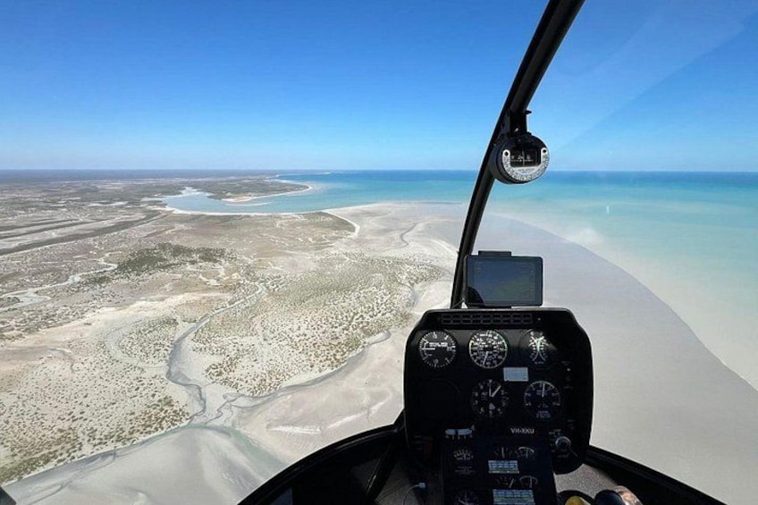 A helicopter cockpit with a view of a coastal landscape, including a beach and a river. 4